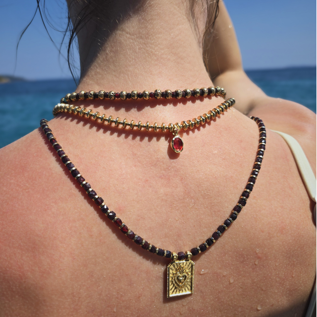 Three layered beaded necklaces with a gold heart pendant, worn on the back against a sea background