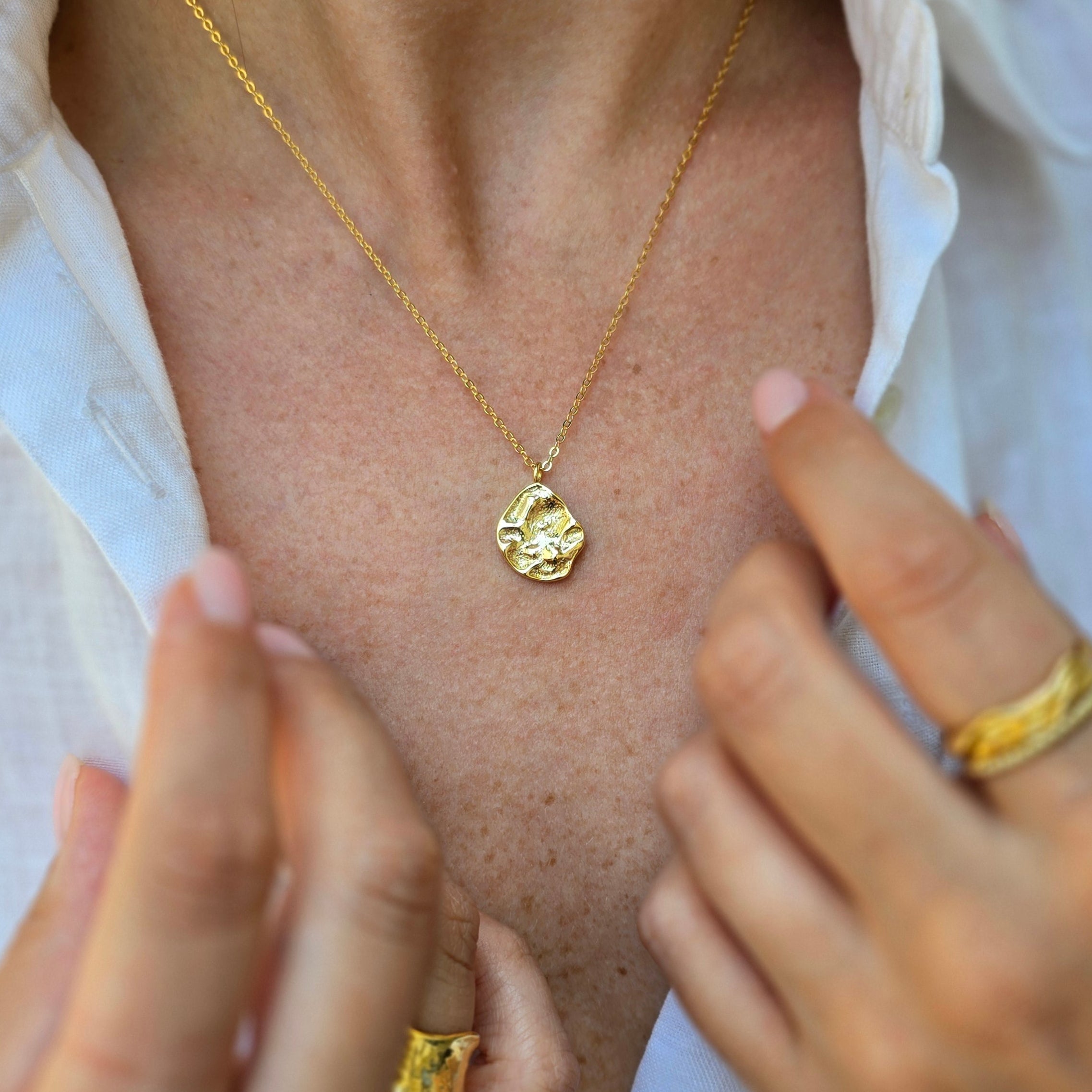 Gold necklace with a pendant being worn on a person's chest.