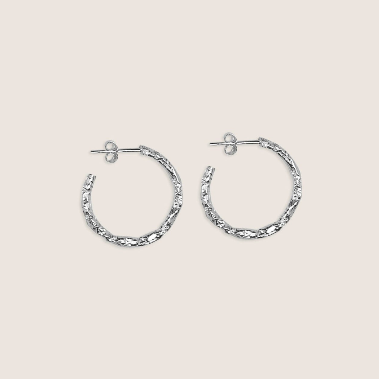 Pair of silver hoop earrings on a light beige background